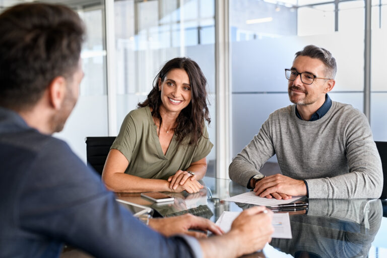 A financial advisor talking with a man and woman sitting across a table during a meeting about inheritance planning.